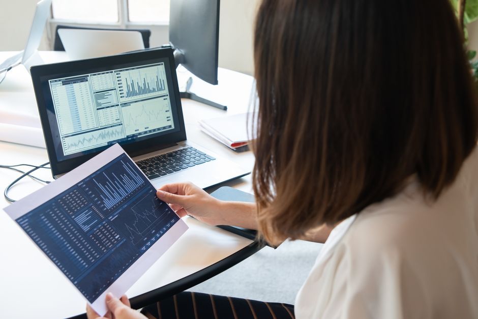 Woman holding a printed chart next to her laptop